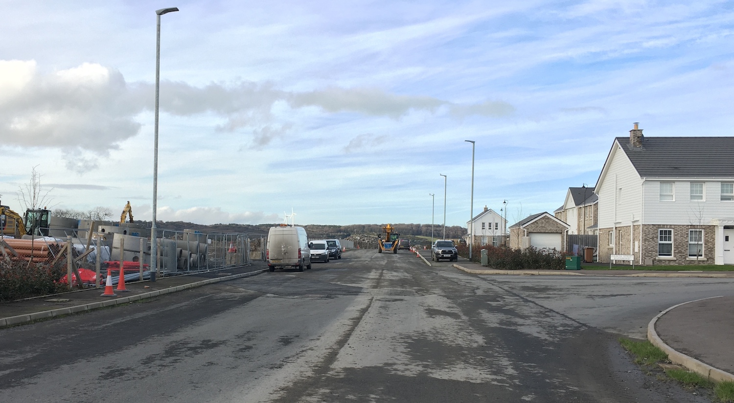 Road ending abruptly at a building site,
with open ground to the left and a new house
on the right.
