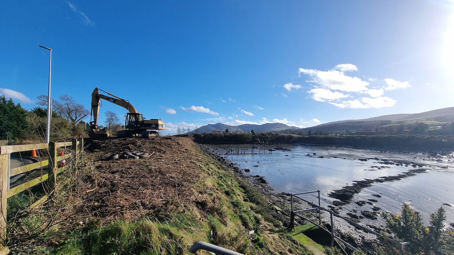 Water on the right, then a coastline in
the centre and on the left is a grassy verge
with a digger moving earth around.