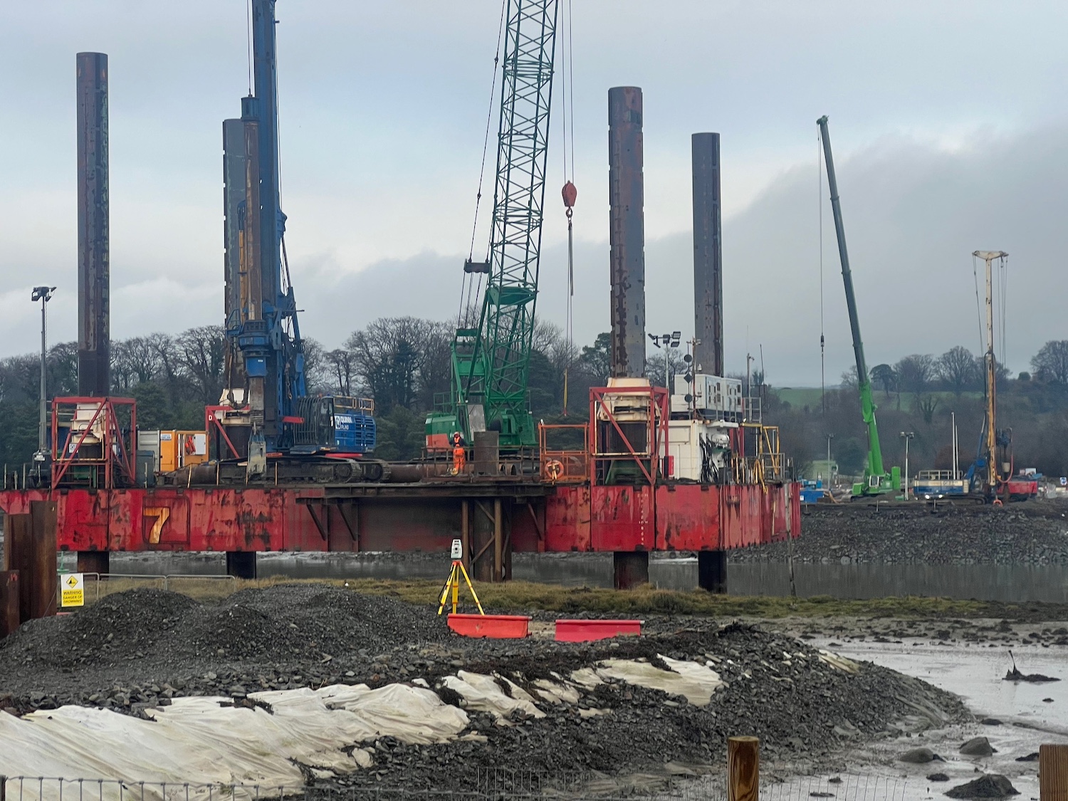 Ground level view of a red platform with
four long legs extending into the air, with a
crane and a pile driver on the platform.