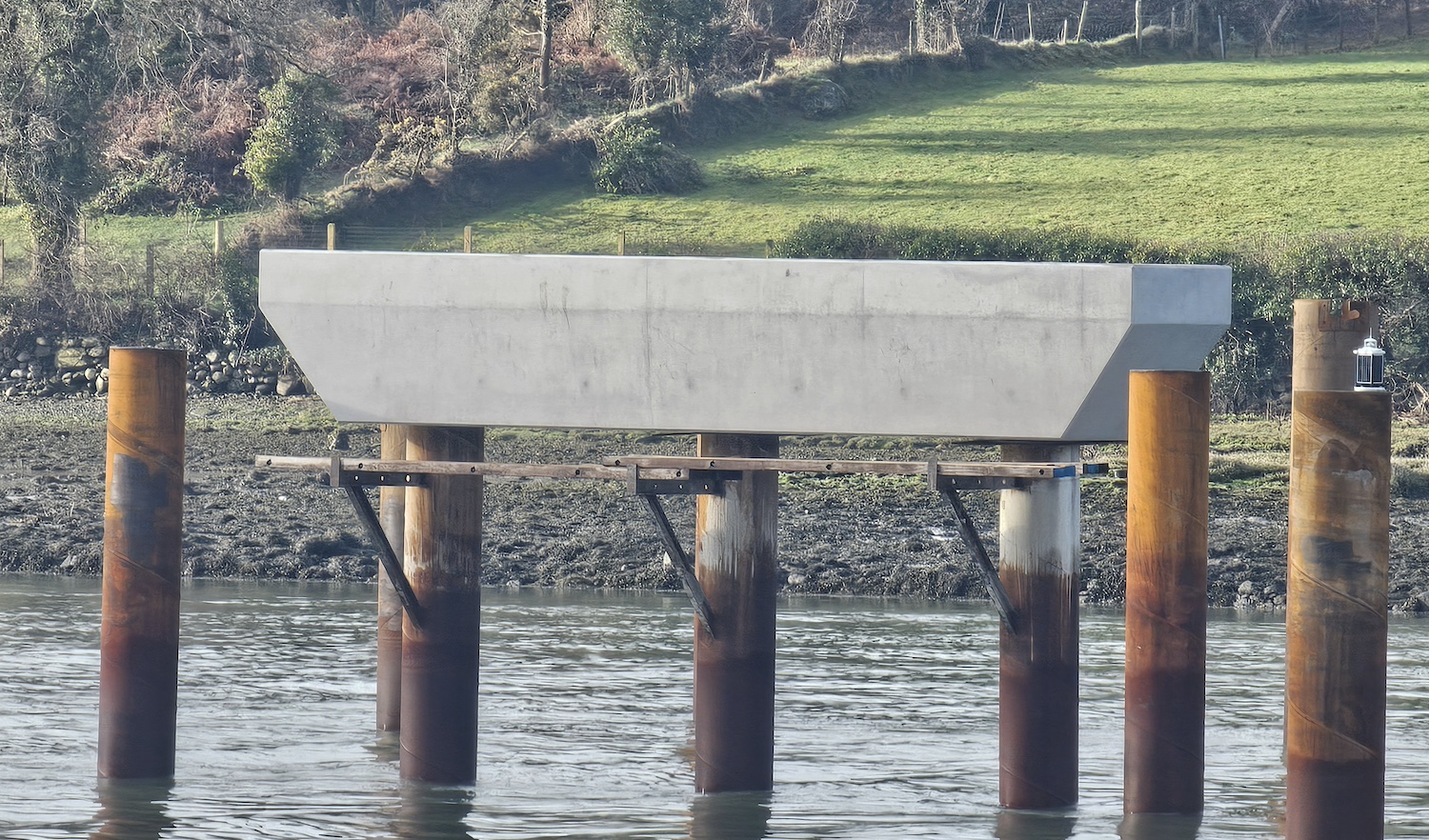 Three round metal piles sticking out of
water with a large, horizontal concrete beam
joining them together at the top.