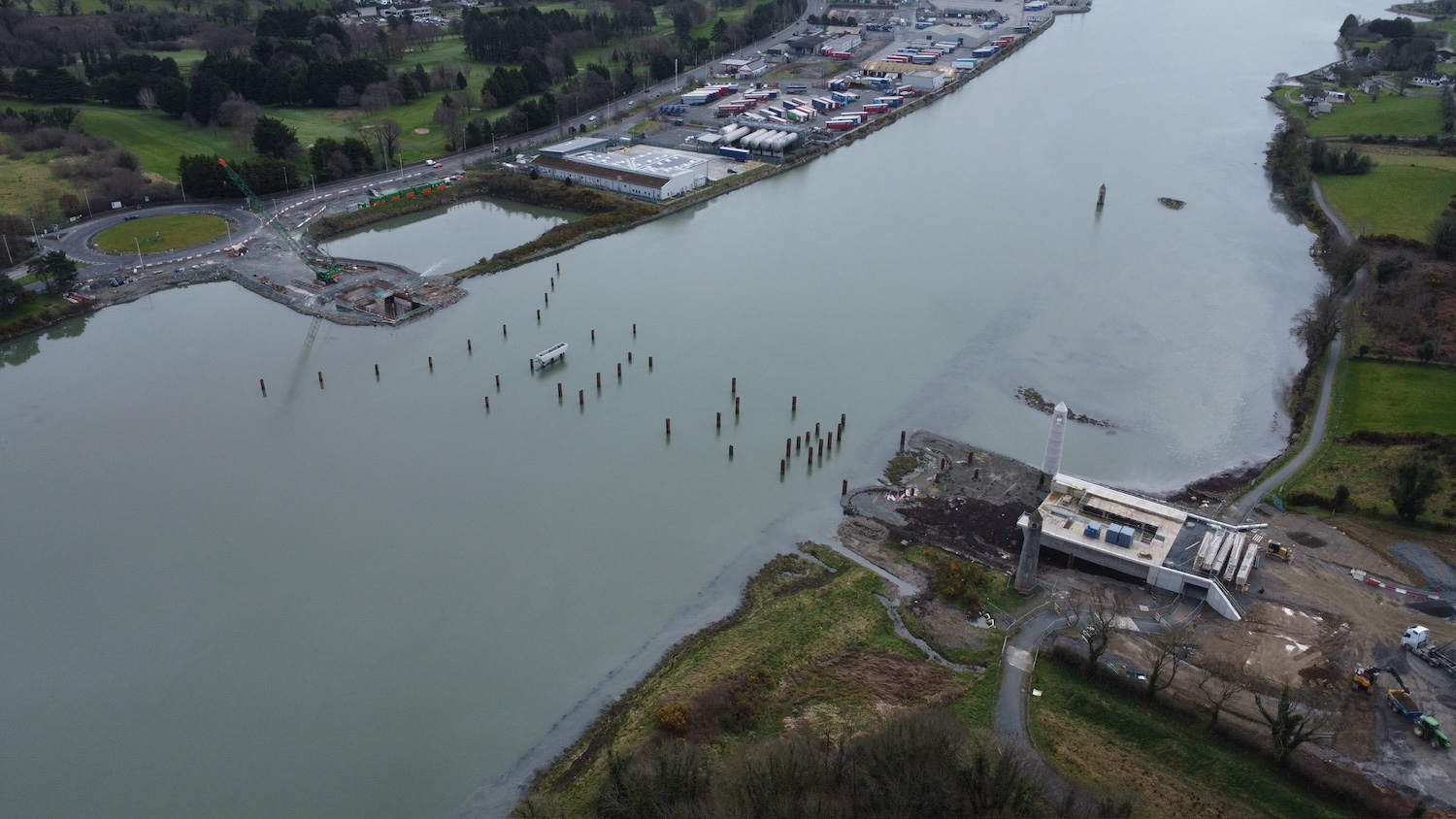 Aerial view with river from bottom left
to top right. Lots of vertical piles evident
in a line between the two abutments which are
under construction.